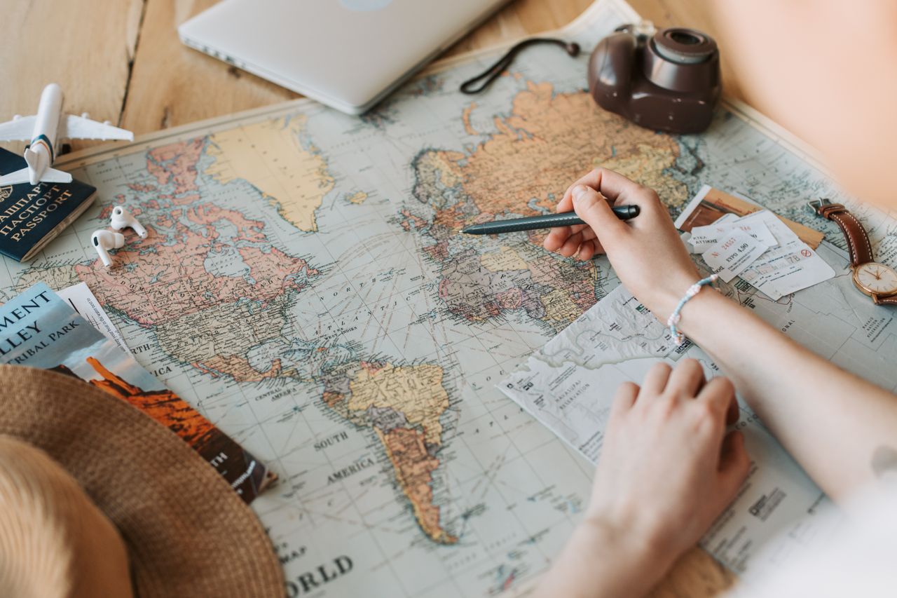 The Art of Drawing Readers In: Your attractive post title goes here Hands marking destinations on a world map surrounded by travel essentials like passport and camera.
